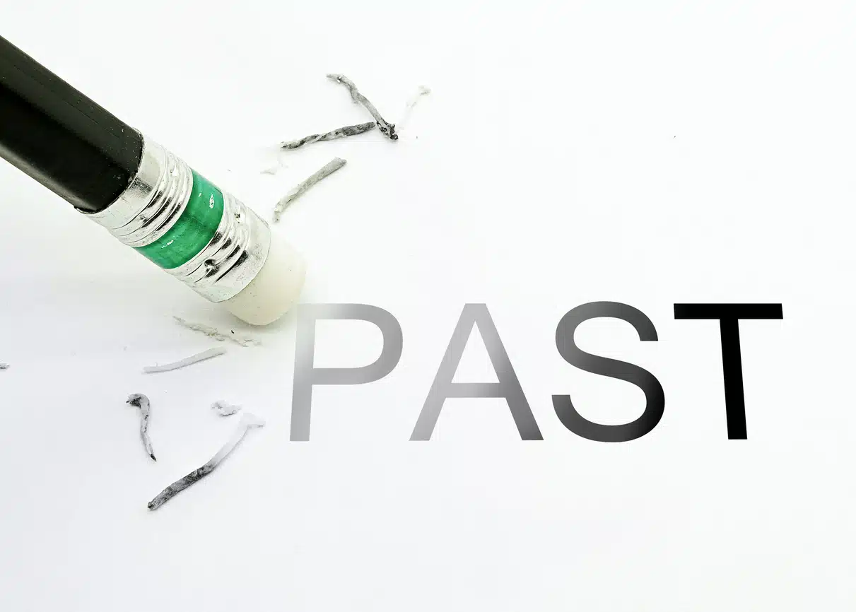 A white eraser tip on a black pencil erases the ‘p’ in ‘past,’ written on a blank paper in all caps.
